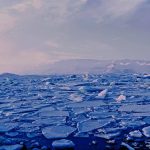 Dos personas en un bloque de hielo observan el derretimiento del mismo en pequeñas fracciones, consecuencia del aumento de las temperaturas.